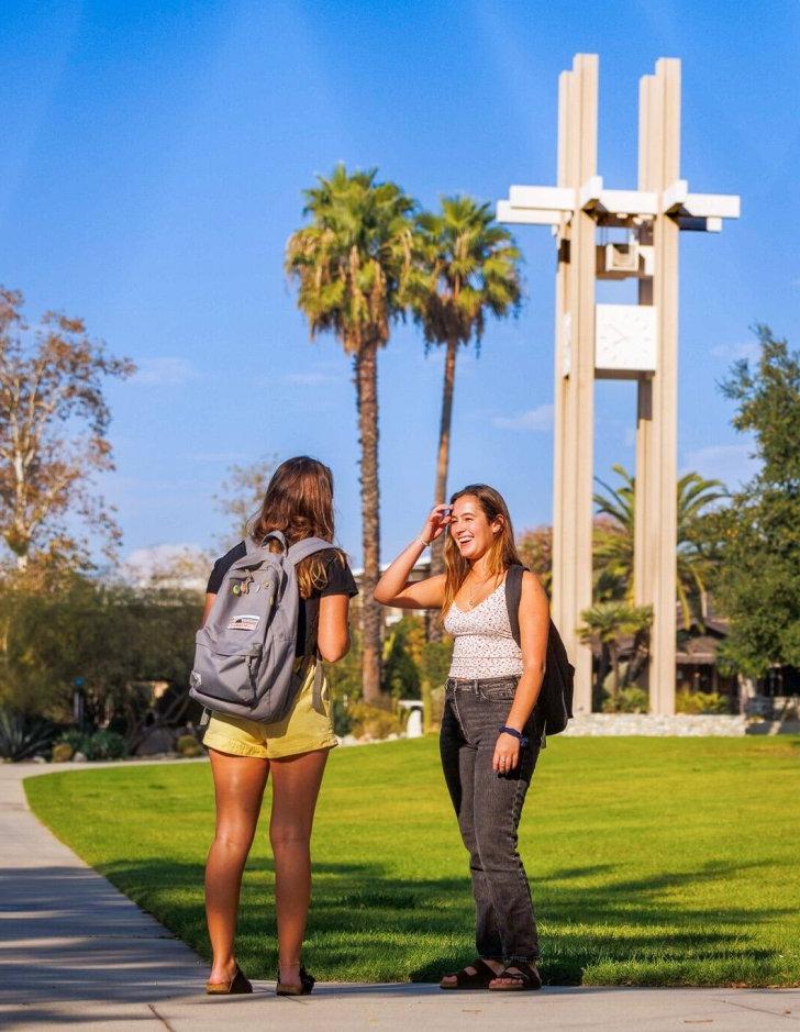 Two students talk with with the clock tower in the background